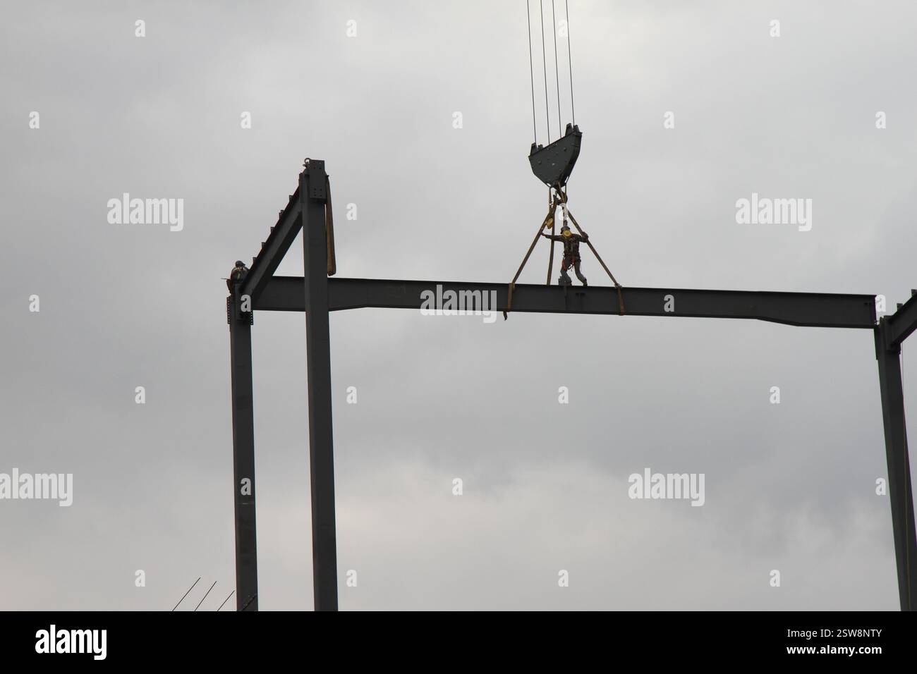 Un ouvrier de construction sur une poutre en acier dans les hauteurs pendant qu'il est transporté par une grue de construction. Un homme travaillant dans la construction. Banque D'Images