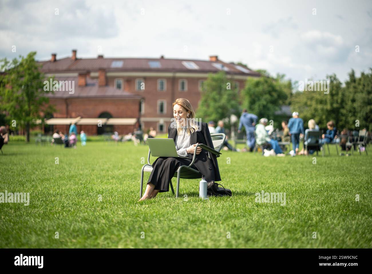 Étudiante ou femme d'affaires assise sur une chaise longue dans le parc avec ordinateur portable, ayant la vidéoconférence. Banque D'Images