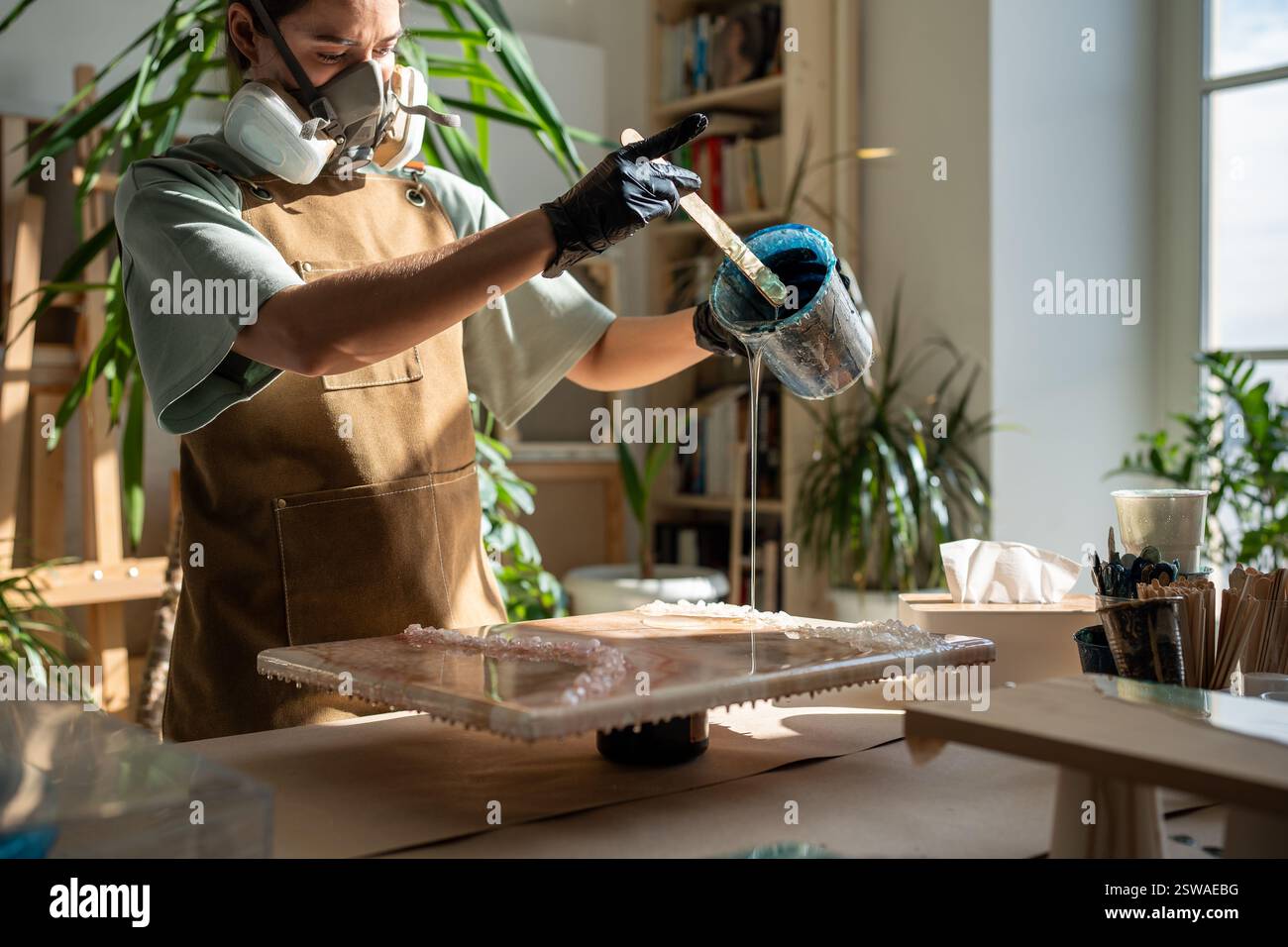 Femme concentrée, artiste liquide créant un motif sur toile tout en travaillant avec la peinture de résine époxy Banque D'Images