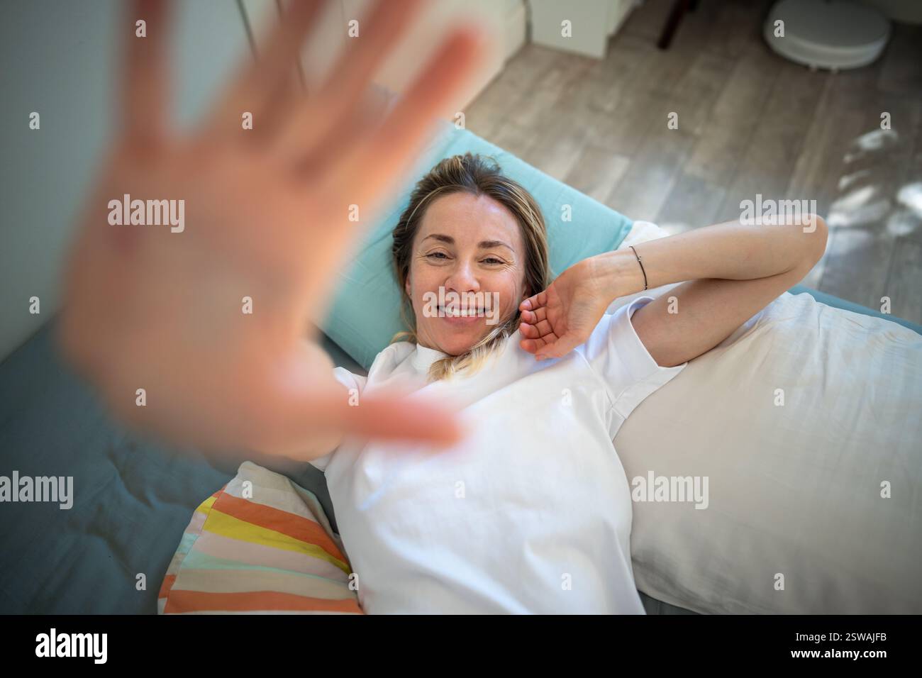 Femme endormie d'âge moyen se trouve sur le lit souriant et s'étirant levé d'une main près de la caméra. Banque D'Images