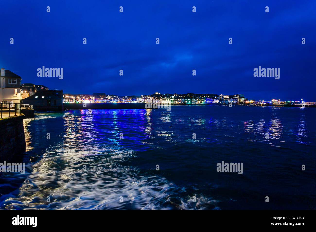 Une vue nocturne pittoresque d'une ville côtière, probablement au Royaume-Uni, reflétée dans les eaux calmes d'un port Banque D'Images