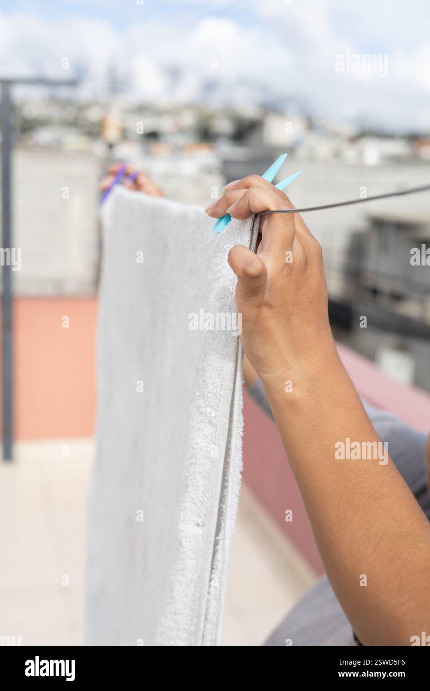 Une personne accrochant une serviette fraîche sur une corde à linge sous le soleil, parfait pour la maison, la lessive et les thèmes de vie en plein air. Banque D'Images