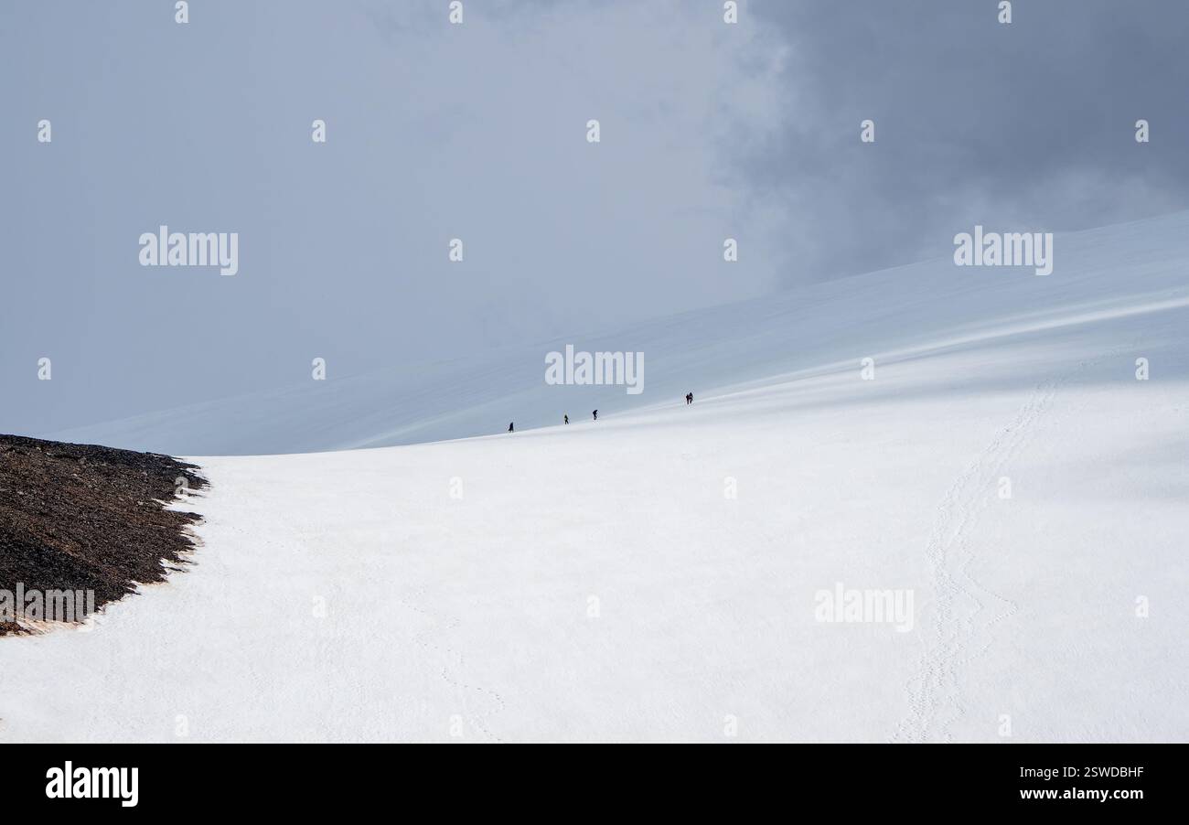 Paysage panoramique minimaliste avec escalade de groupe sur une grande montagne enneigée à la lumière du soleil sous ciel nuageux. Paysage atmosphérique w Banque D'Images
