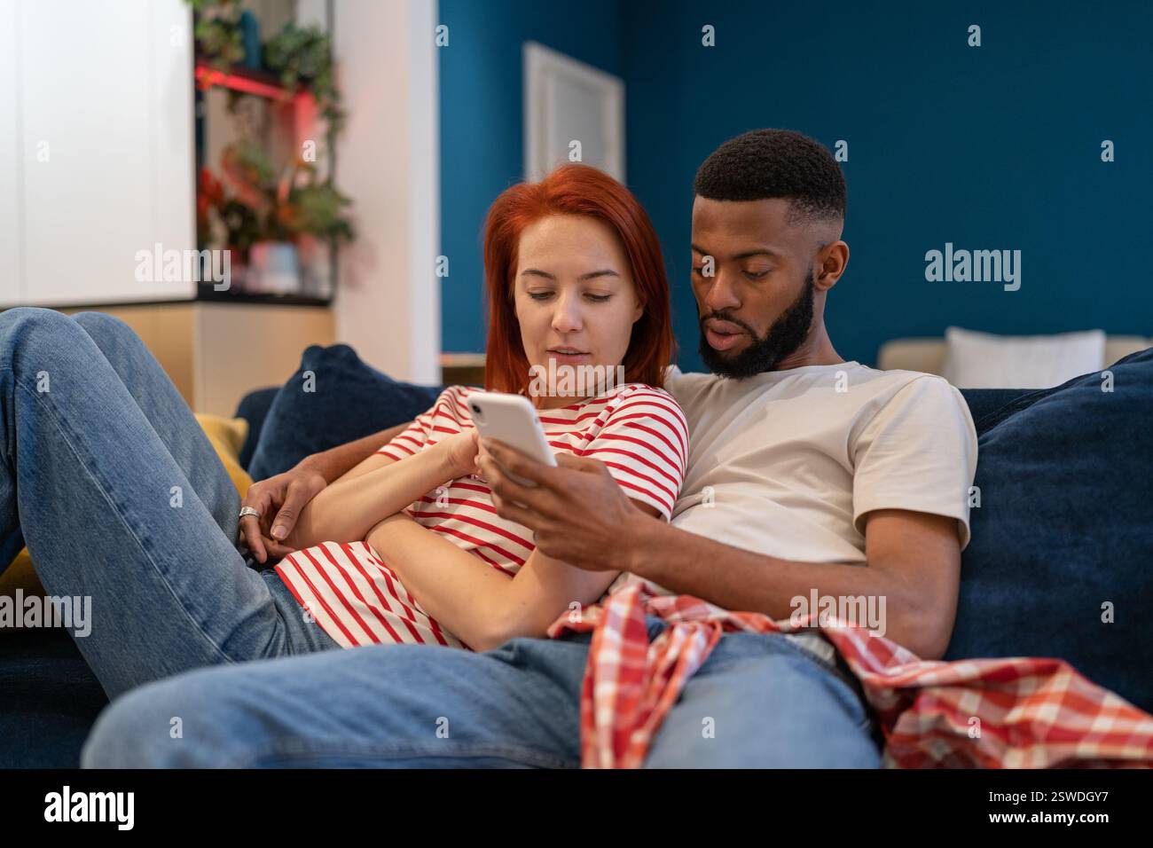 Jeune millénaire couple divers homme et femme se reposant à la maison avec le téléphone mobile Banque D'Images