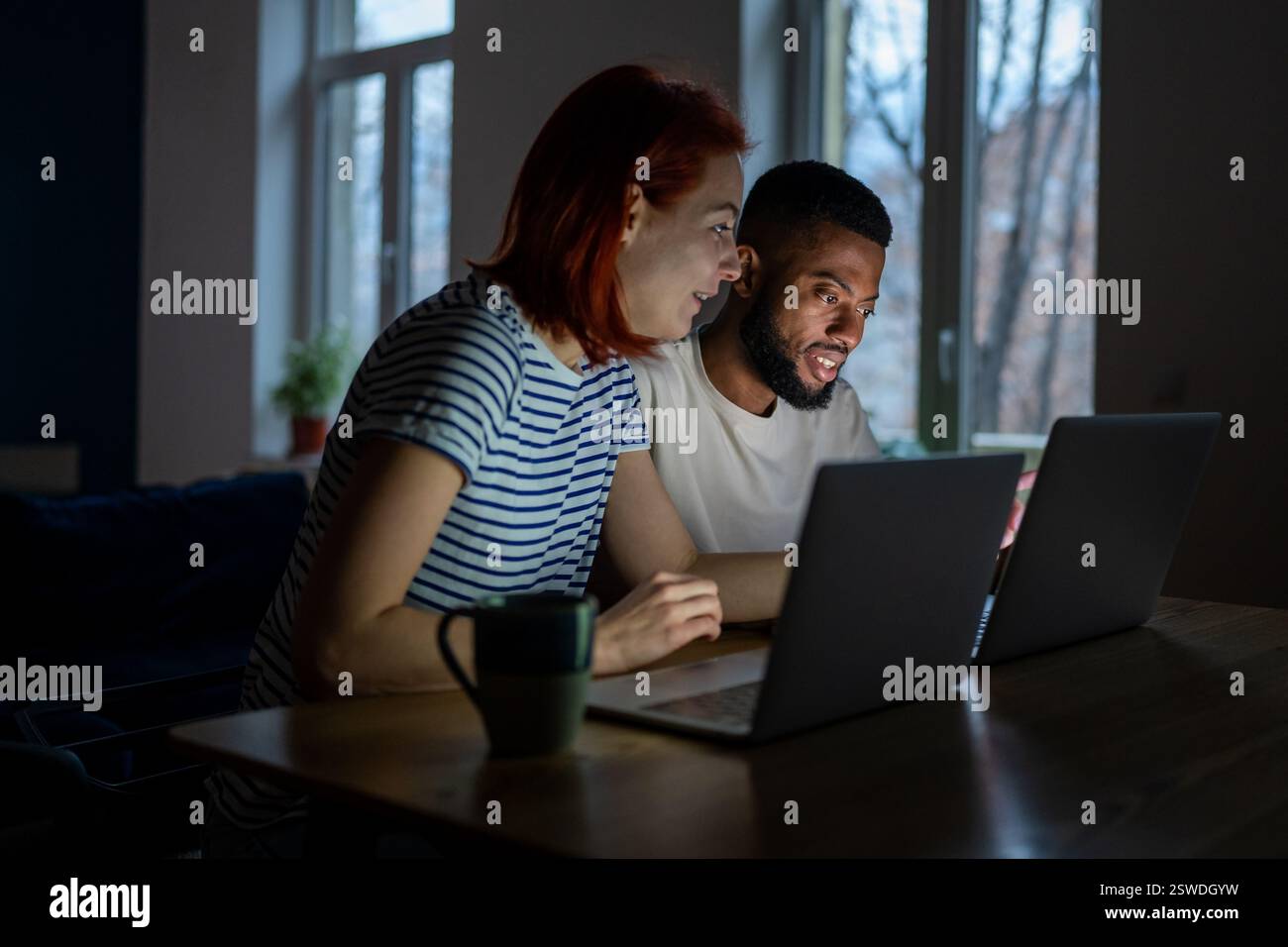 Heureux couple diversifié ont de petites affaires en ligne au travail à la maison sur les ordinateurs portables en soirée Banque D'Images