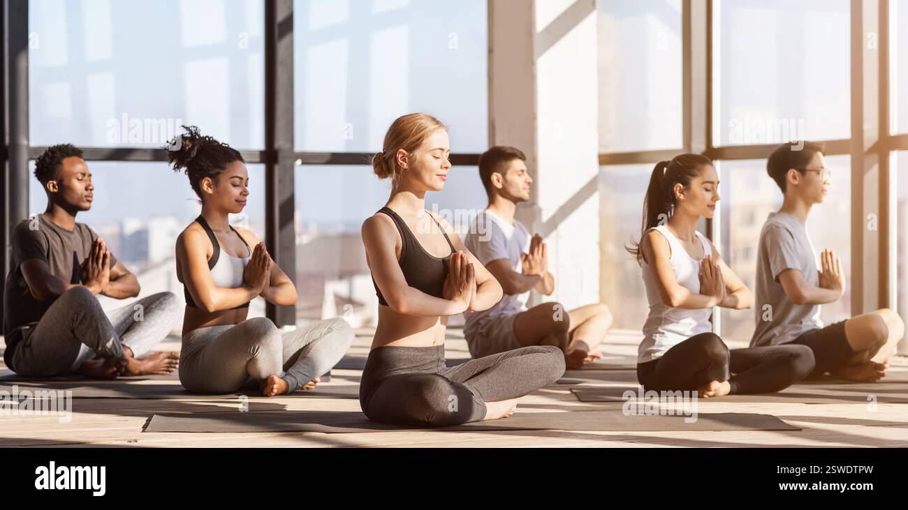 Session de méditation. Groupe de sportifs divers pratiquant le yoga dans la salle de gym moderne Banque D'Images