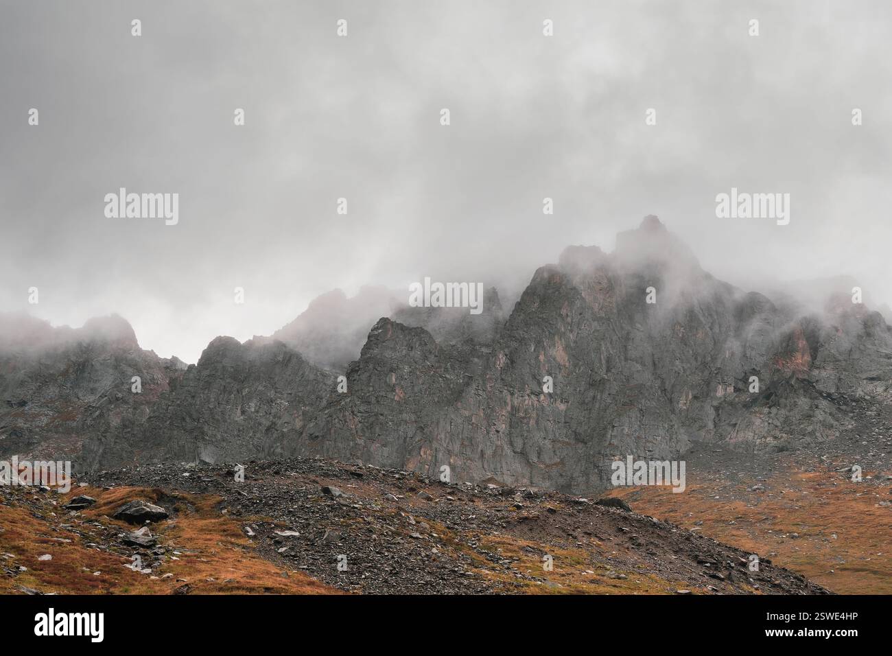 Paysage brumeux atmosphérique avec des silhouettes floues de roches acérées dans les nuages bas pendant la pluie. Vue spectaculaire sur les grandes montagnes bl Banque D'Images