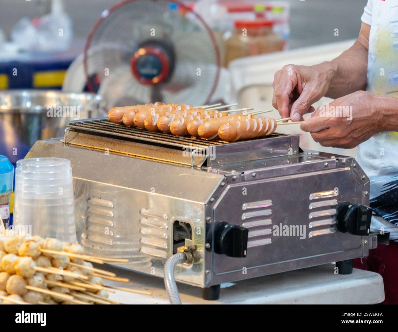 Le fournisseur fait griller la saucisse sur le gril du marché de l'alimentation de rue. Banque D'Images