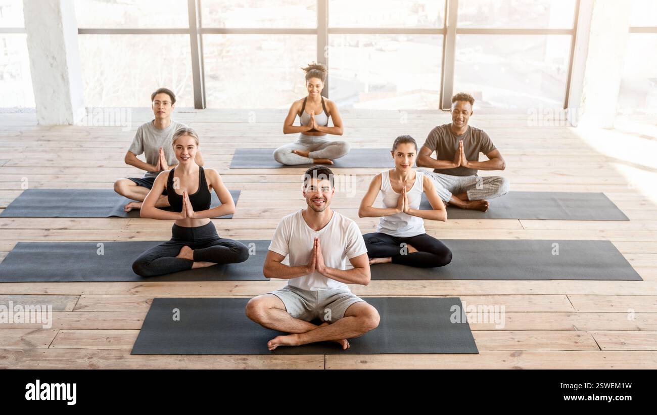 Divers sportifs assistant à des cours de yoga en studio, assis en position lotus Banque D'Images