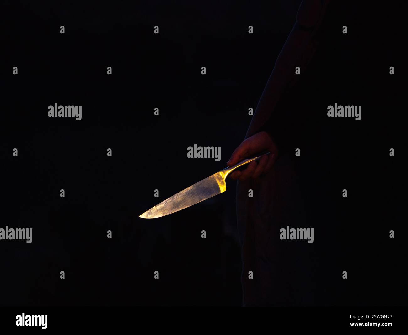 Grande lame de couteau brillante à la main sur un fond sombre. Banque D'Images