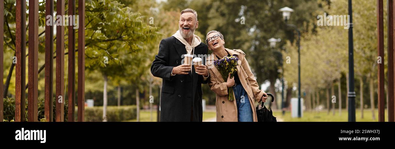 Un couple joyeux profite de boissons chaudes tout en se promenant dans un parc paisible rempli de verdure. Banque D'Images