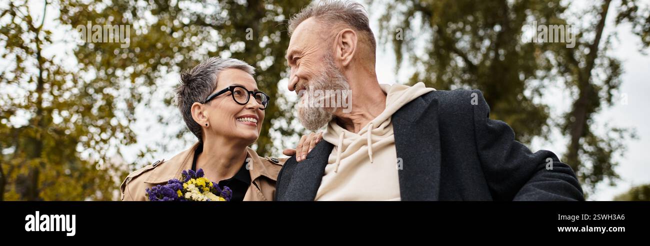 Un couple mûr profite d'une promenade paisible ensemble, partageant des sourires et tenant des fleurs vibrantes. Banque D'Images