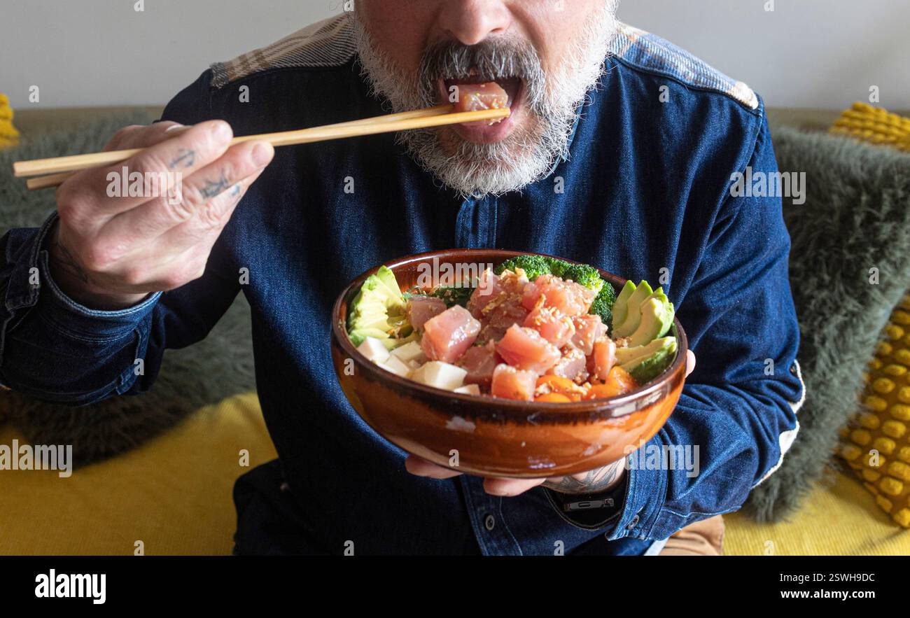 Homme barbu appréciant un bol de poke sain avec des baguettes Banque D'Images