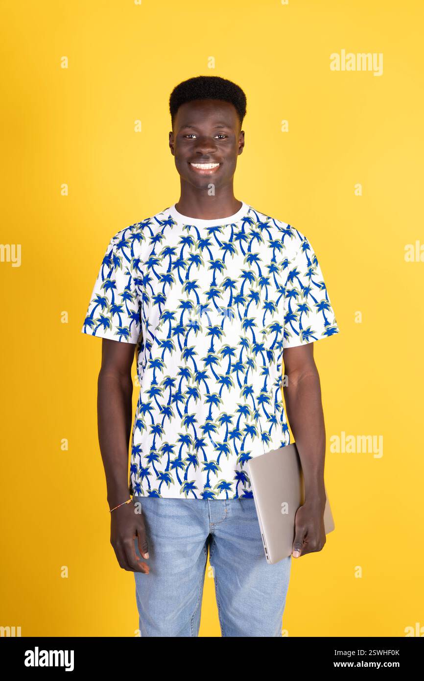 Un jeune homme portant une chemise avec des palmiers dessus tient un ordinateur portable. Il sourit et il est heureux Banque D'Images