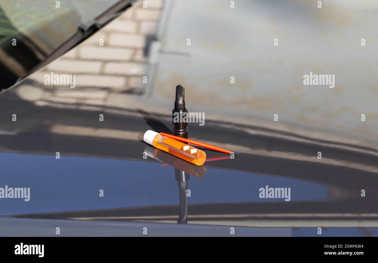 Une boîte de peinture noire, convertisseur de rouille et un pinceau sur le capot d'une voiture. Concept pour enlever les éclats de la peinture sur une voiture, gros plan Banque D'Images