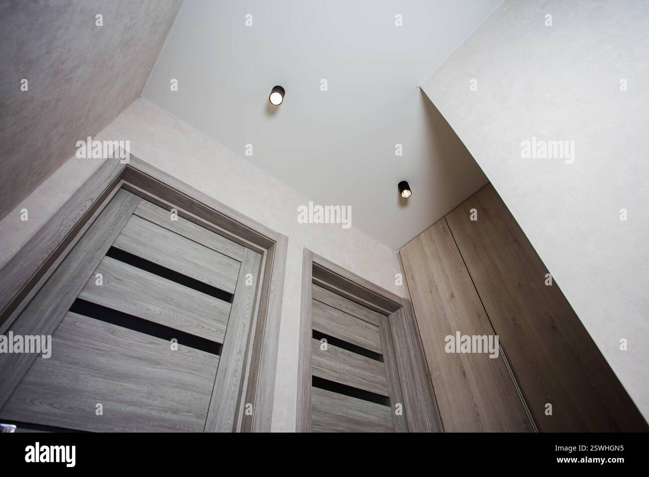 Deux portes intérieures grises modernes pour l'entrée de la chambre avec pour toile de fond une armoire intégrée et un plafond suspendu avec des lampes dans le hal Banque D'Images