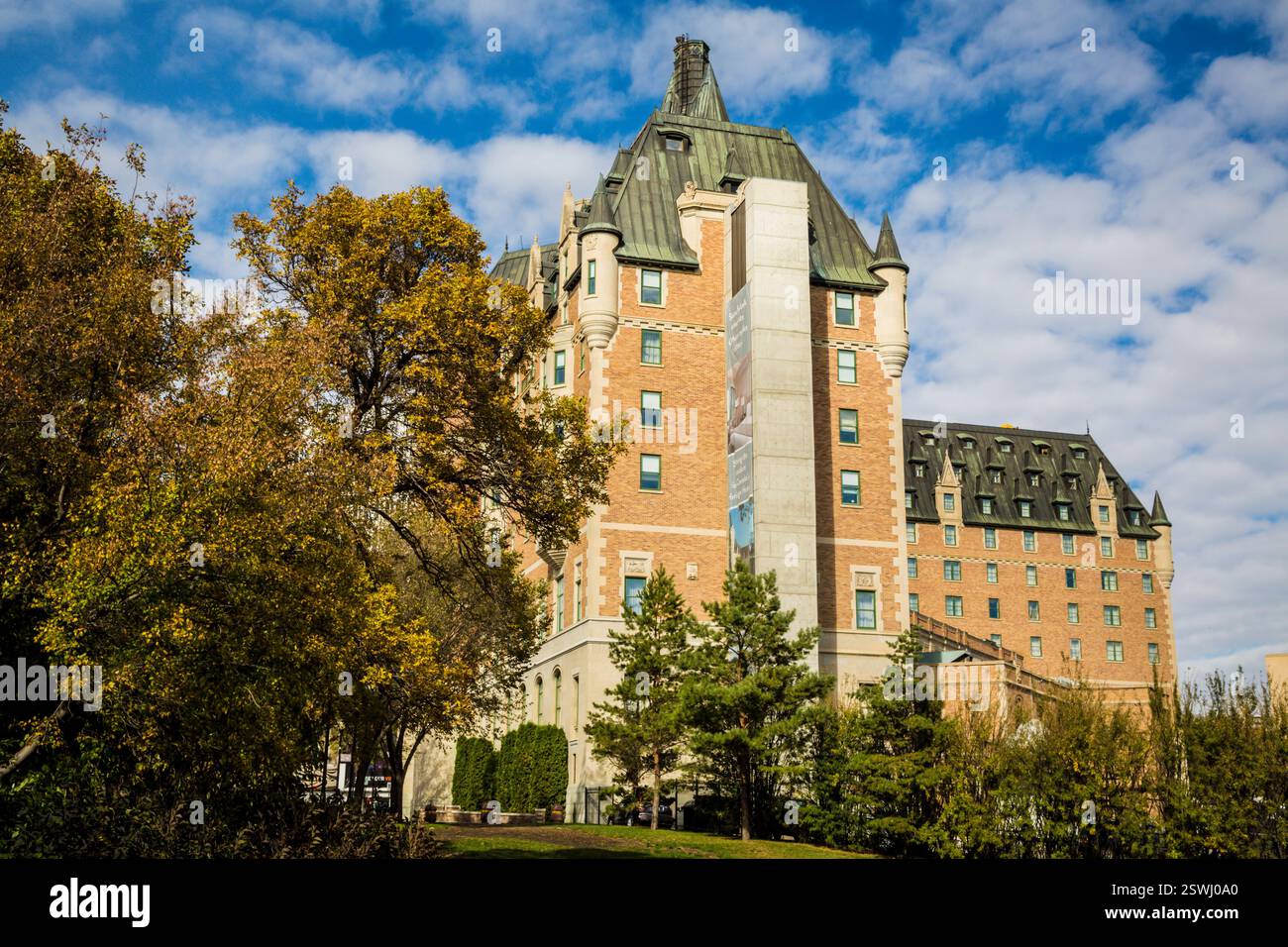 Grand bâtiment en briques avec un toit vert. Le bâtiment a une tour de l'horloge. Le bâtiment est entouré d'arbres Banque D'Images