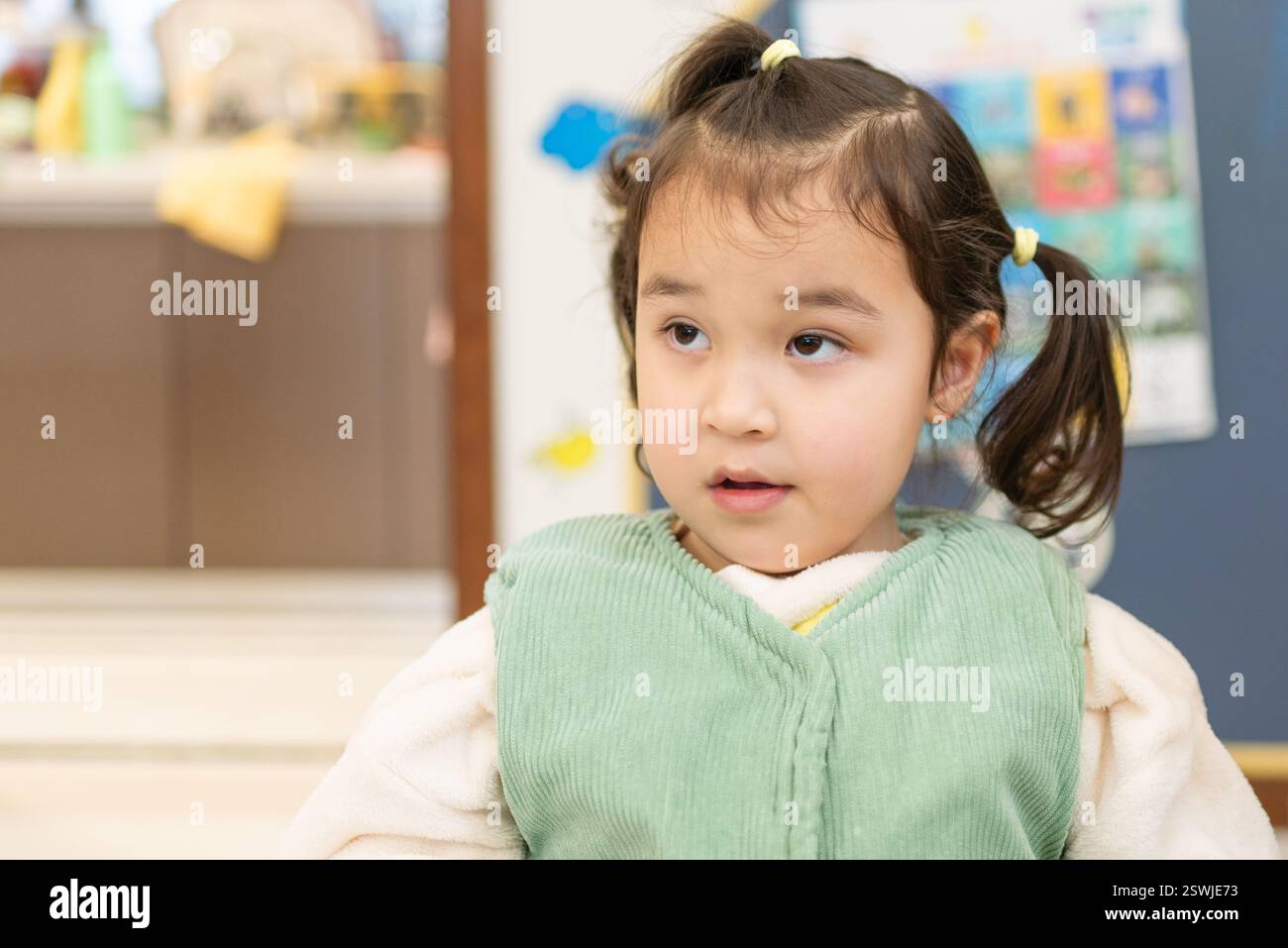 Une fille multiraciale est assise dans le salon, attendant patiemment le petit déjeuner. Ses cheveux sont attachés avec de petites attaches colorées. Banque D'Images