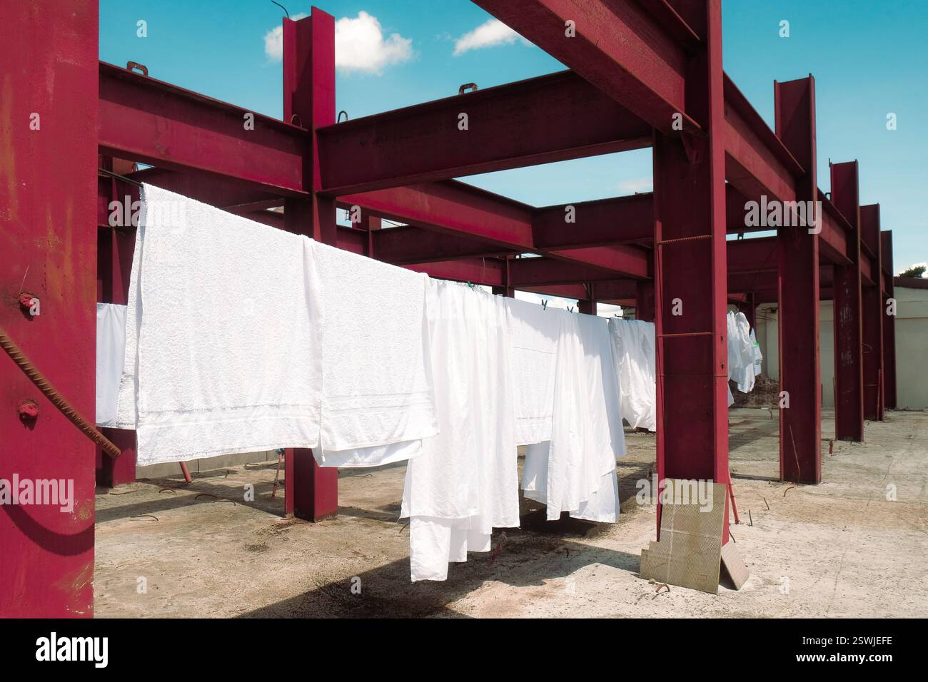 Des feuilles blanches fraîches sèchent à l'air sur une corde à linge au-dessus d'un bâtiment industriel avec des barres d'acier rouges. Ciel bleu jour ensoleillé. Contexte du service de blanchisserie de l'hôtel Banque D'Images