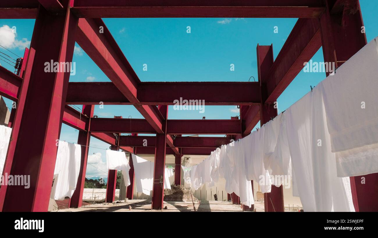 Des feuilles blanches fraîches sèchent à l'air sur une corde à linge au-dessus d'un bâtiment industriel avec des barres d'acier rouges. Ciel bleu jour ensoleillé. Contexte du service de blanchisserie de l'hôtel Banque D'Images