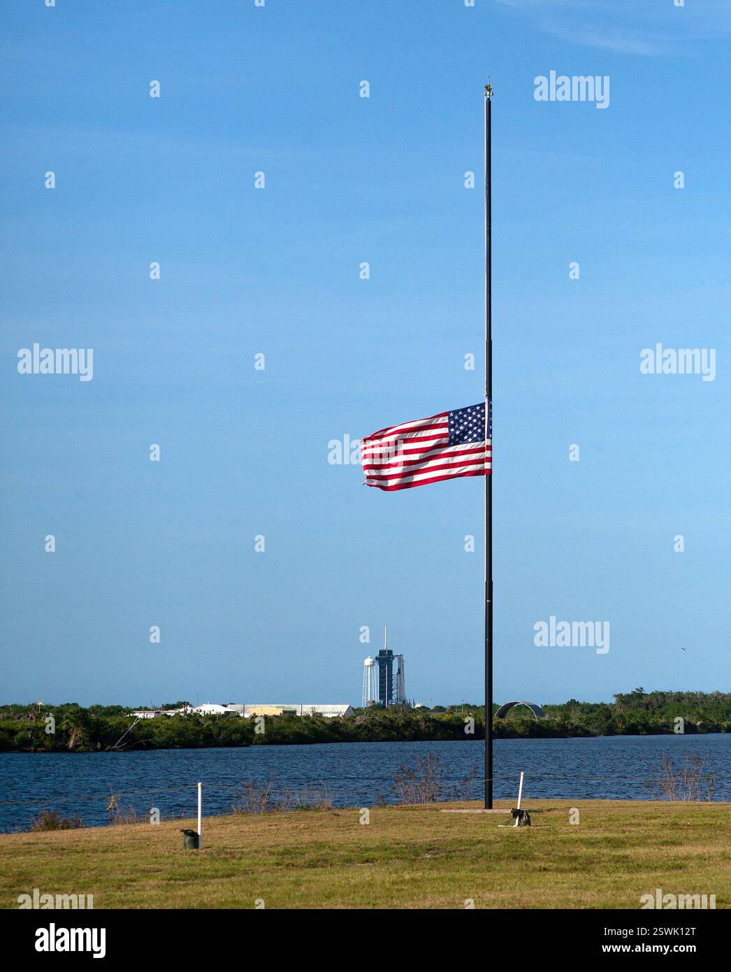 Le drapeau américain flotte à moitié à côté de l'horloge du compte à rebours au Kennedy Space Center le 22 mai 2020 pendant la pandémie de coronavirus. Au loin, la mission SpaceX Demo-2 de la NASA se prépare à un vol d'essai. Banque D'Images