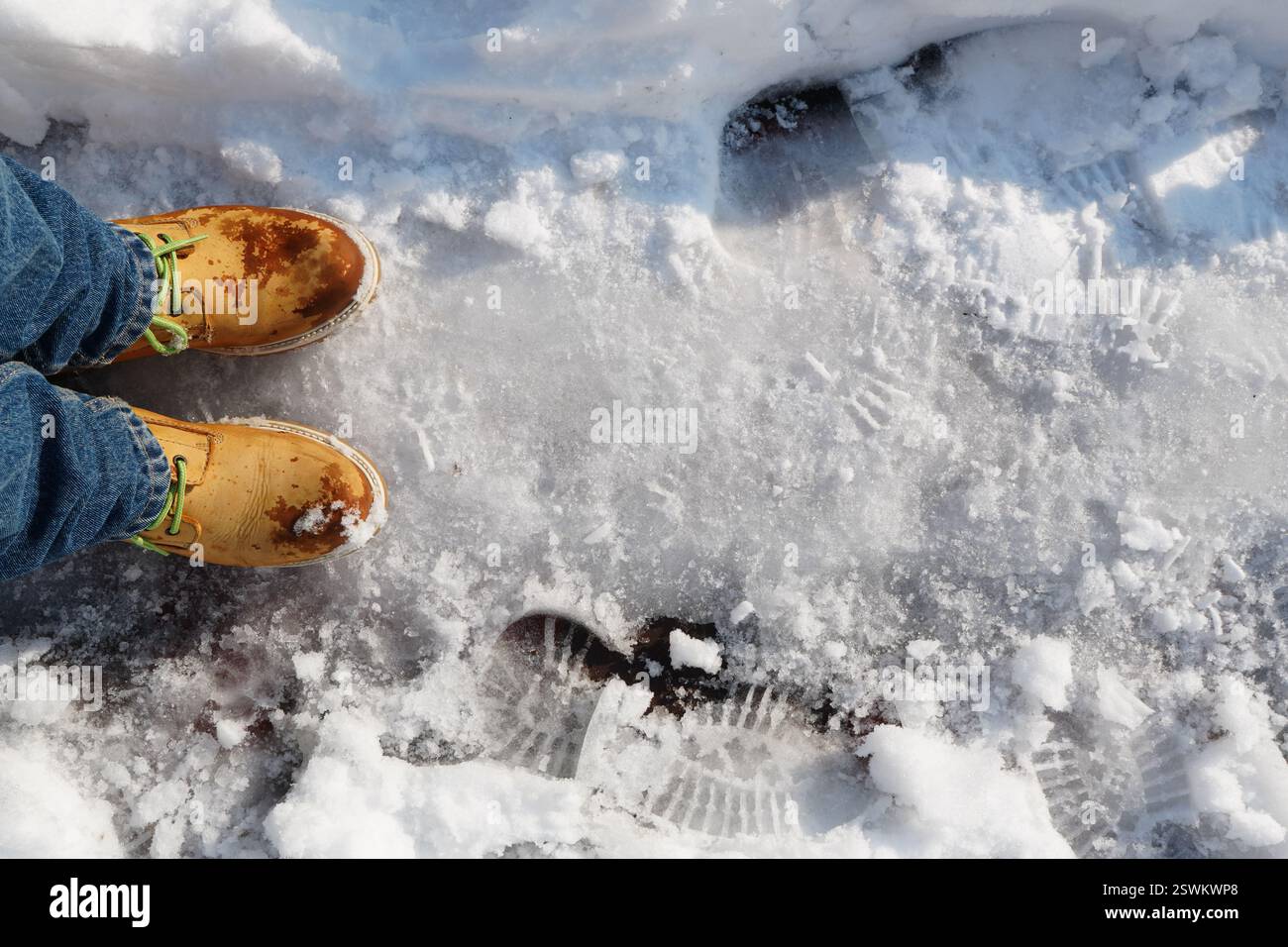 Marchez sur le sentier de neige battu sur le trottoir portant des bottes jaunes avec des lacets verts et des jeans bleus à la lumière du soleil en hiver Banque D'Images