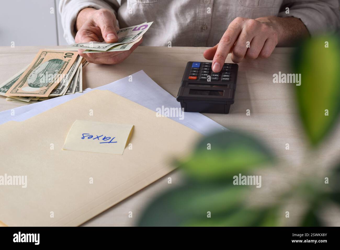 Femme assise à un bureau comptant des dollars américains en argent comptant avec une calculatrice faisant des impôts Banque D'Images