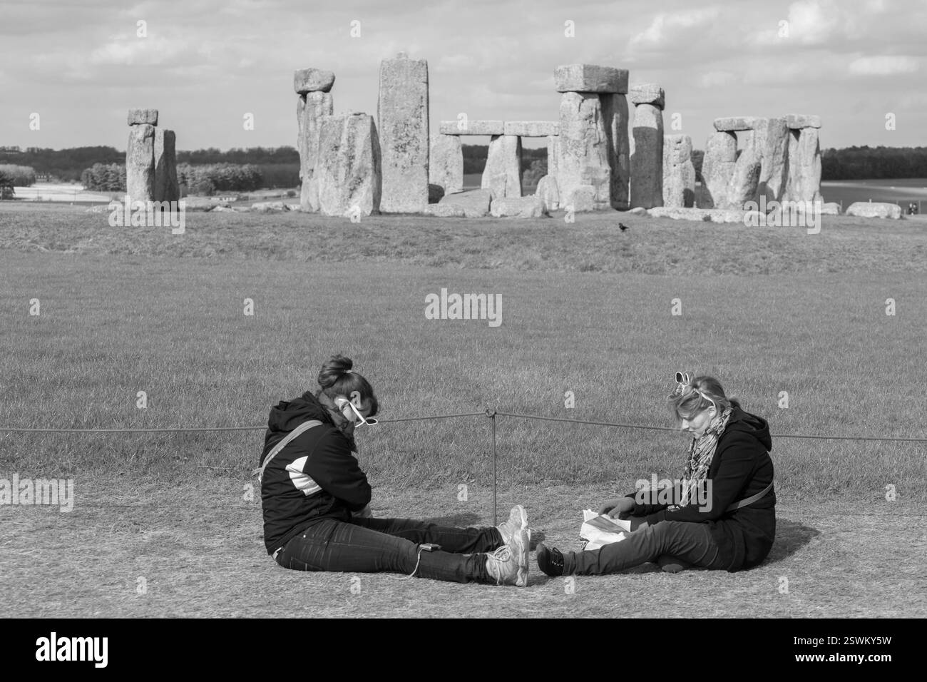 Deux femmes sont assises près de Stonehenge, Wiltshire, Angleterre, observant l'ancien cercle de pierre. Banque D'Images