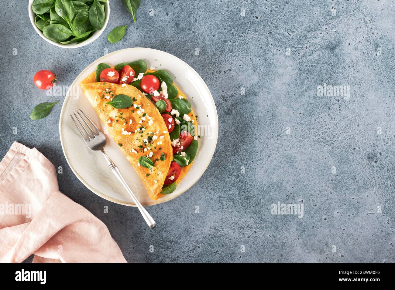 Omelette farcie aux tomates, fromage et épinards sur fond bleu. Vue de dessus. Copier l'espace. Banque D'Images