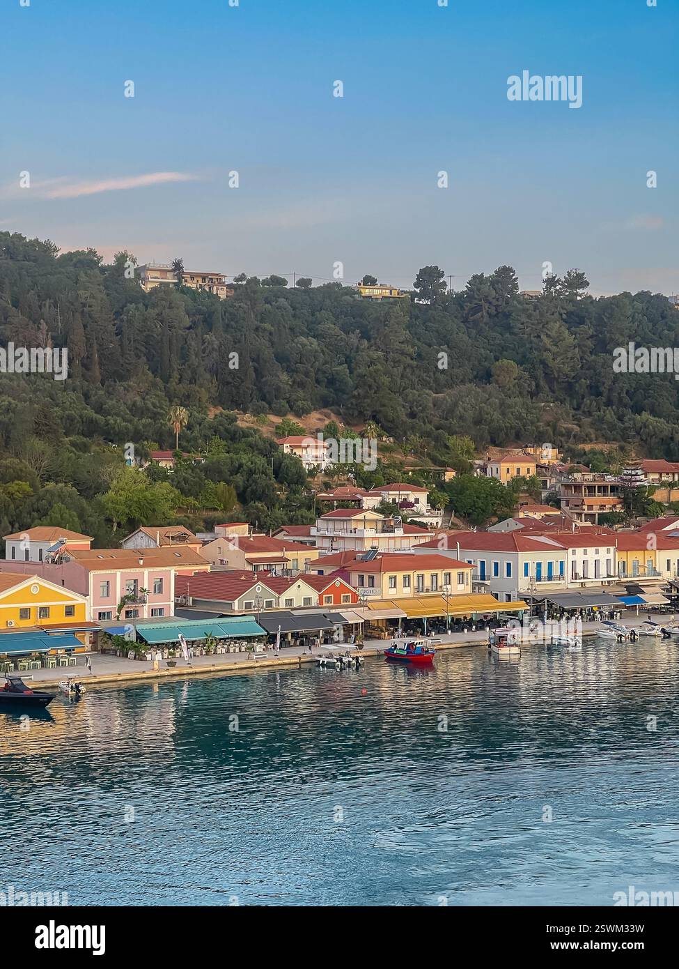 Katakolo, Grèce - 4 juillet 2024 : promenade commerciale dans le port de plaisance avec principalement des restaurants et des bistros. Rangée de façades colorées, colline verte à l'arrière Banque D'Images
