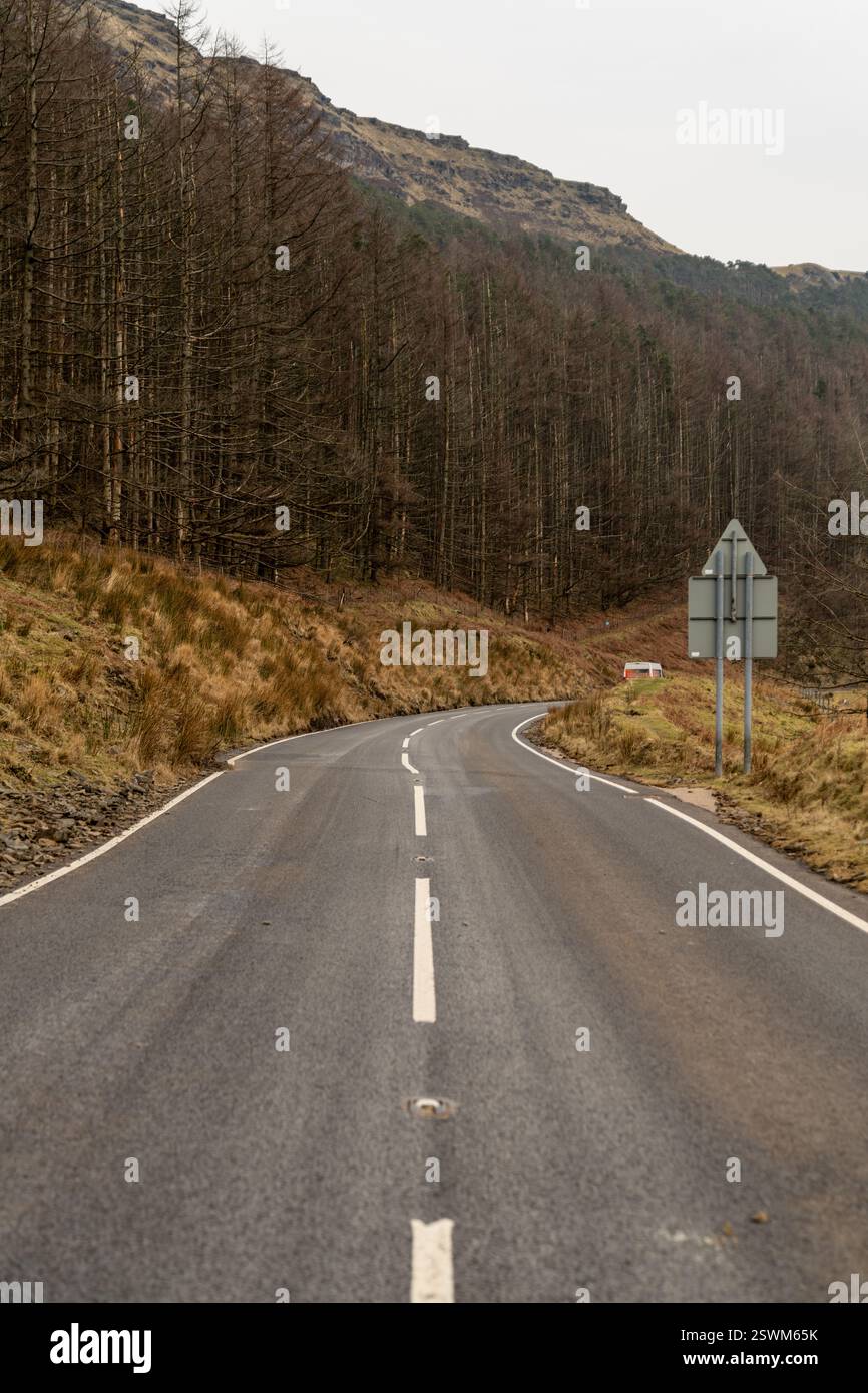 Une route rurale sinueuse avec une double ligne blanche, entourée d'arbres arides et de collines. Banque D'Images