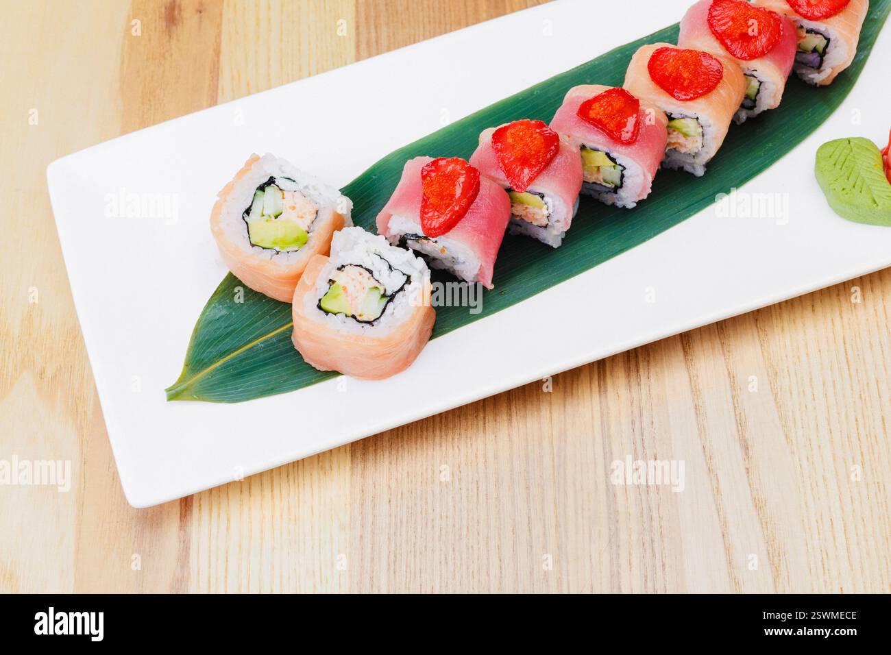 Plateau de sushi coloré avec divers rouleaux et garnitures fraîches servies sur une feuille Banque D'Images