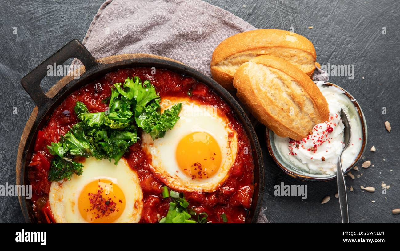 Oeufs Shakshuka dans une casserole avec du pain sur un fond sombre. Oeufs pochés dans une sauce épicée au poivre tomate. Œufs brouillés juifs traditionnels. Vue de dessus. PA Banque D'Images