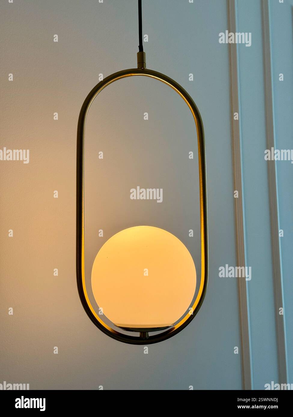 Suspension dorée avec sphère lumineuse moderne Une suspension minimaliste dotée d'un cadre en métal doré et d'une sphère en verre opale éclatante - Image de stock capturée avec un smartphone