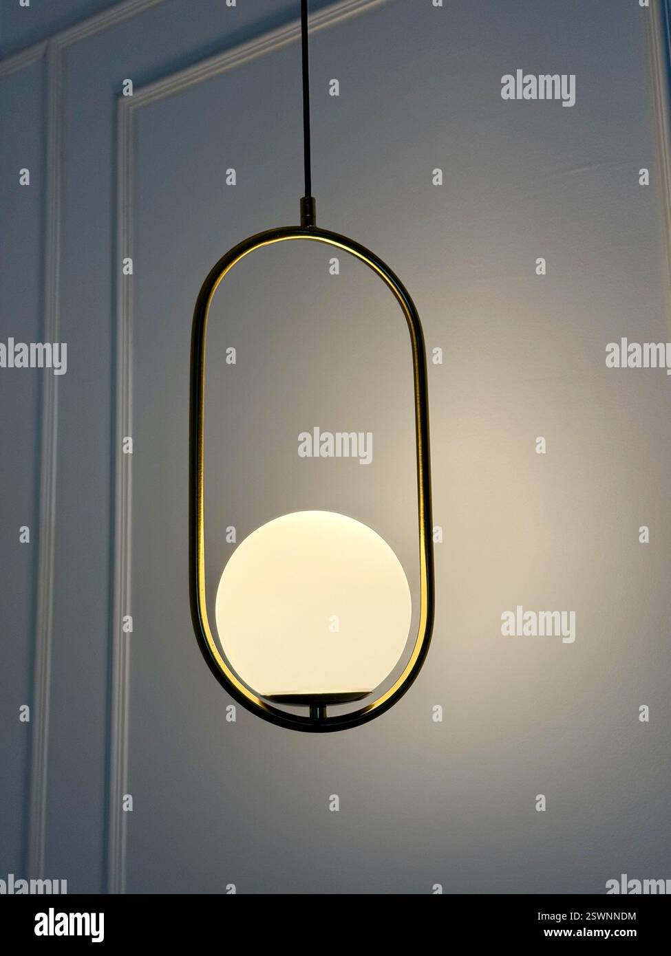 Suspension dorée avec sphère lumineuse moderne Une suspension minimaliste dotée d'un cadre en métal doré et d'une sphère en verre opale éclatante, projetant un Sof - Image de stock capturée avec un smartphone