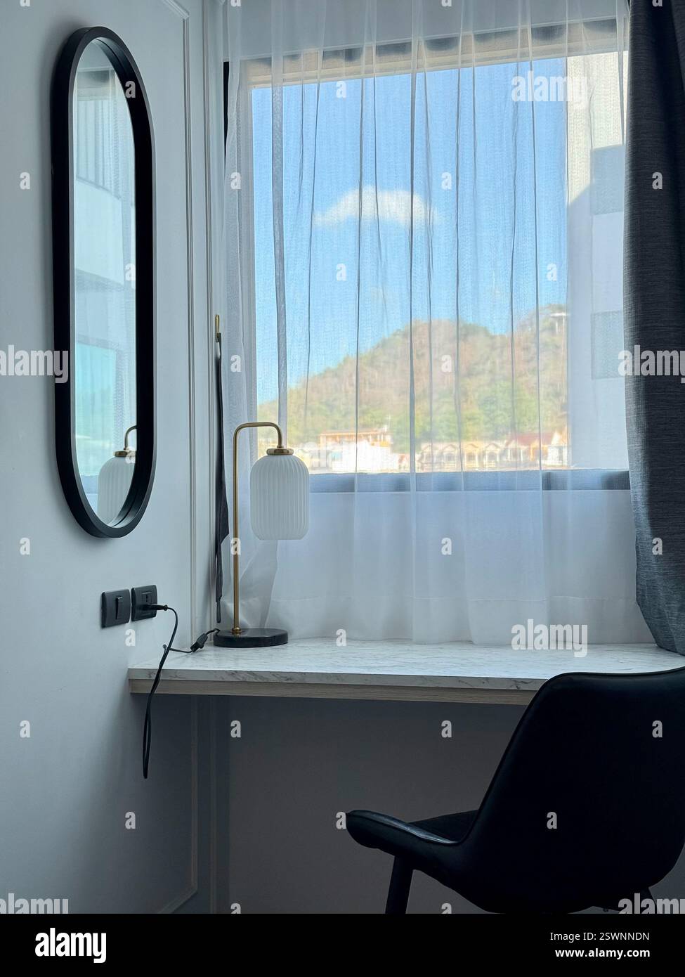 Bureau minimaliste avec vue sur la ville et la colline Un bureau moderne en marbre blanc placé devant une grande fenêtre avec des rideaux transparents Banque D'Images