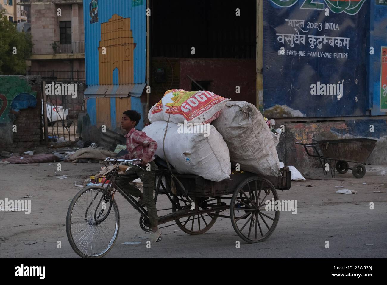 Un enfant ouvrier cycle une charge de déchets à recycler près d'un hangar avec la porte de l'Inde peinte dessus à New Delhi, en Inde Banque D'Images