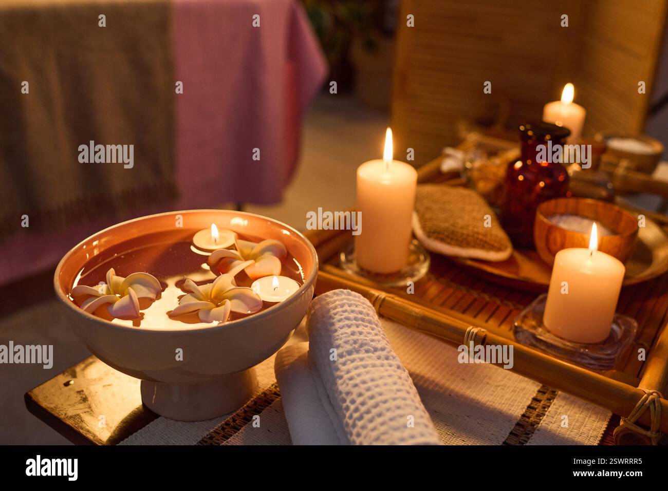 Plan à angle élevé de table basse en bois avec bol en céramique rempli d'eau pure et de bourgeons de fleurs, plateau avec bougies d'arôme allumées Banque D'Images