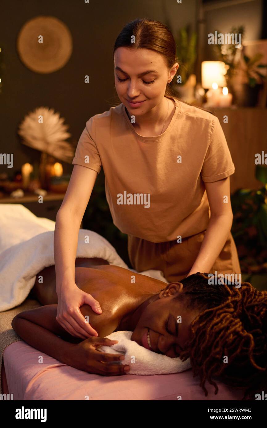 Plan vertical de femme afro-américaine allongée sur la table de massage tout en profitant d'un merveilleux massage relaxant par masseuse professionnelle Banque D'Images