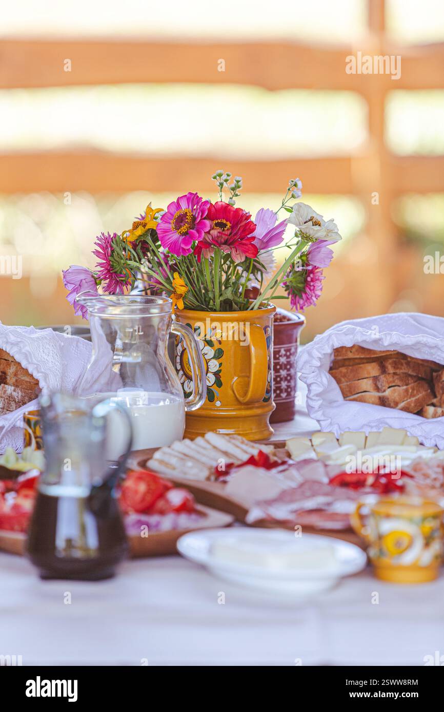 Une table de petit déjeuner magnifiquement dressée avec fleurs fraîches, fromages, légumes et boissons. Banque D'Images