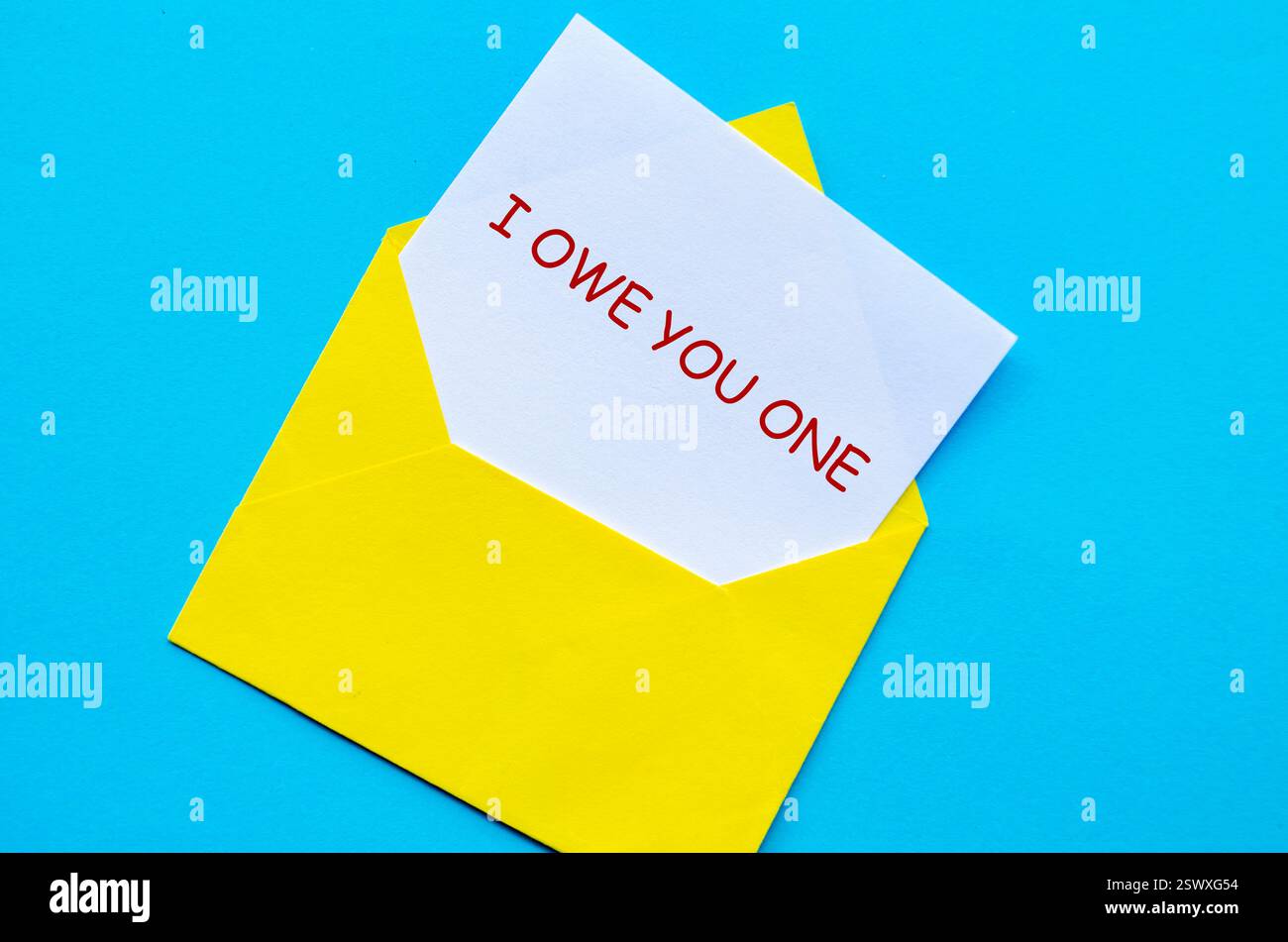 Enveloppe jaune sur une couverture bleue avec une carte blanche partiellement retirée avec je vous dois un texte. Banque D'Images