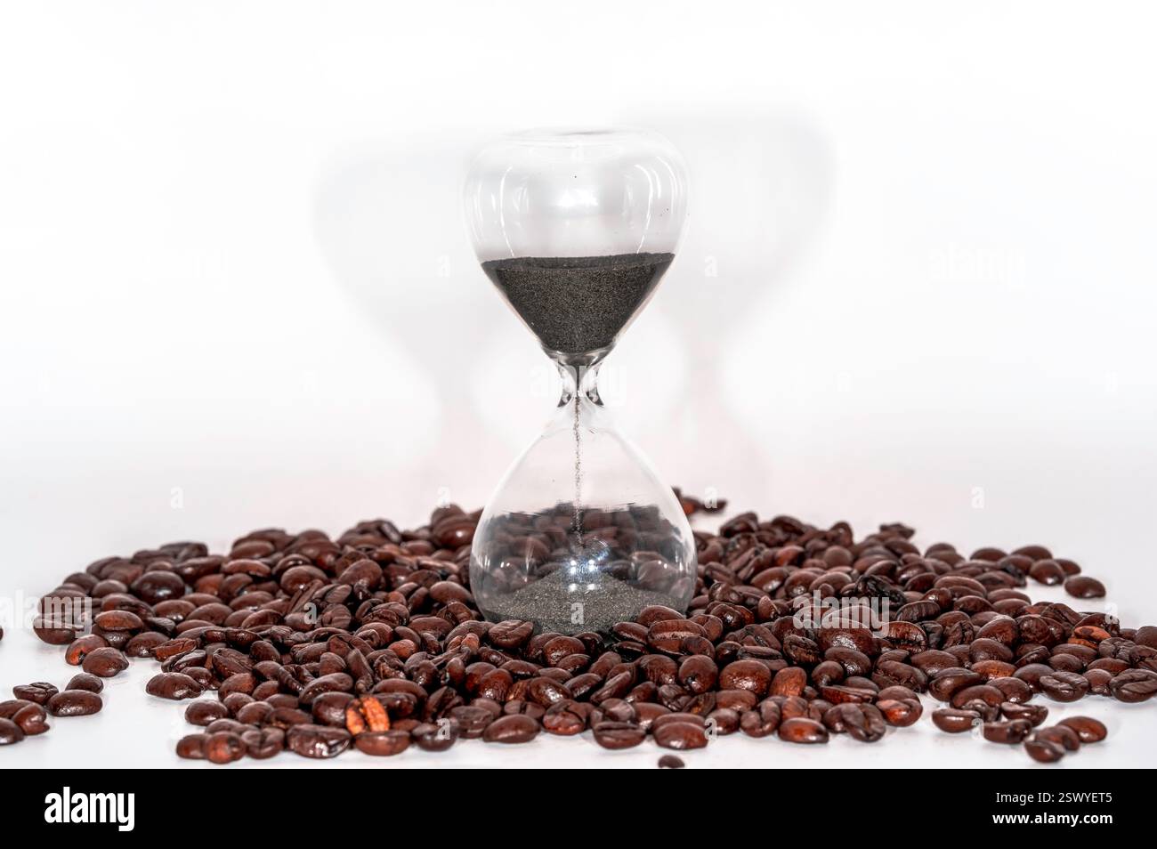 Minuterie sablier en verre avec sable noir entouré de grains de café torréfiés sur un fond blanc Banque D'Images