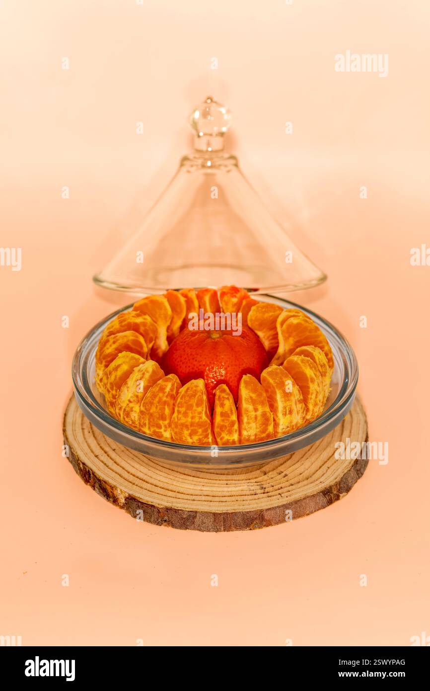 Segments d'orange mandarine pelés et disposés dans un bol en verre sur une tranche de bois avec un dôme en verre dans une composition minimaliste de nature morte Banque D'Images Segments d'orange mandarine pelés et disposés dans un bol en verre sur une tranche de bois avec un dôme en verre dans une composition minimaliste de nature morte Banque D'Images