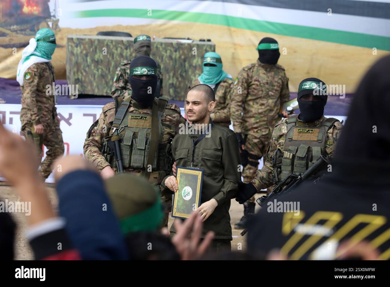Gaza. 22 février 2025. Des membres des Brigades Al-Qassam, la branche armée du Hamas, et un otage israélien sont vus lors de la remise de trois otages israéliens au Comité international de la Croix-Rouge, dans le camp de réfugiés d’al-Nuseirat, dans le centre de Gaza, le 22 février 2025. Six otages israéliens précédemment détenus par le Hamas ont été libérés samedi dans le cadre d’un échange de cessez-le-feu en cours, ont confirmé les Forces de défense israéliennes (FDI) dans un communiqué. Crédit : Rizek Abdeljawad/Xinhua/Alamy Live News Banque D'Images Gaza. 22 février 2025. Des membres des Brigades Al-Qassam, la branche armée du Hamas, et un otage israélien sont vus lors de la remise de trois otages israéliens au Comité international de la Croix-Rouge, dans le camp de réfugiés d’al-Nuseirat, dans le centre de Gaza, le 22 février 2025. Six otages israéliens précédemment détenus par le Hamas ont été libérés samedi dans le cadre d’un échange de cessez-le-feu en cours, ont confirmé les Forces de défense israéliennes (FDI) dans un communiqué. Crédit : Rizek Abdeljawad/Xinhua/Alamy Live News Banque D'Images
