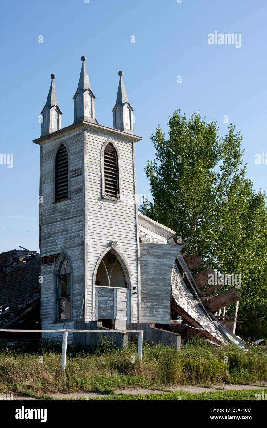Clocher d'église avec un toit cassé et un grand arbre devant lui. L'église est vieille et abandonnée Banque D'Images