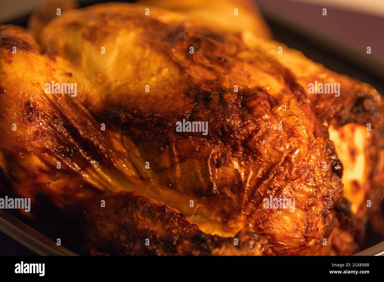 Gros plan détaillé d'un poulet rôti brun doré à la peau croustillante et texturée, soulignant sa couleur riche et son aspect juteux. Banque D'Images