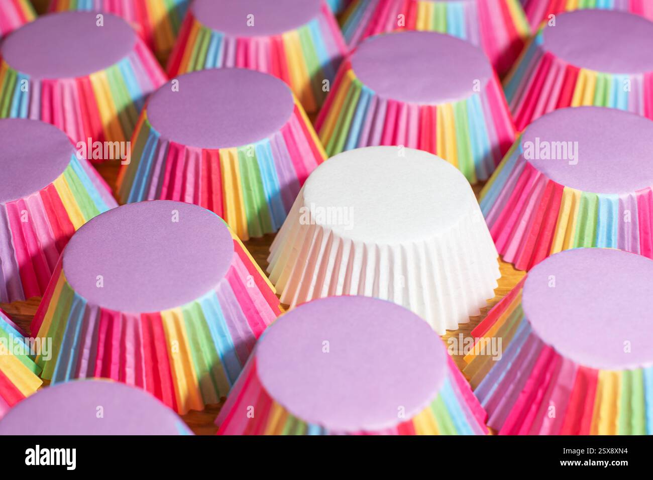 Tasse de muffin blanc unique parmi de nombreuses tasses arc-en-ciel. Concept de différence Banque D'Images