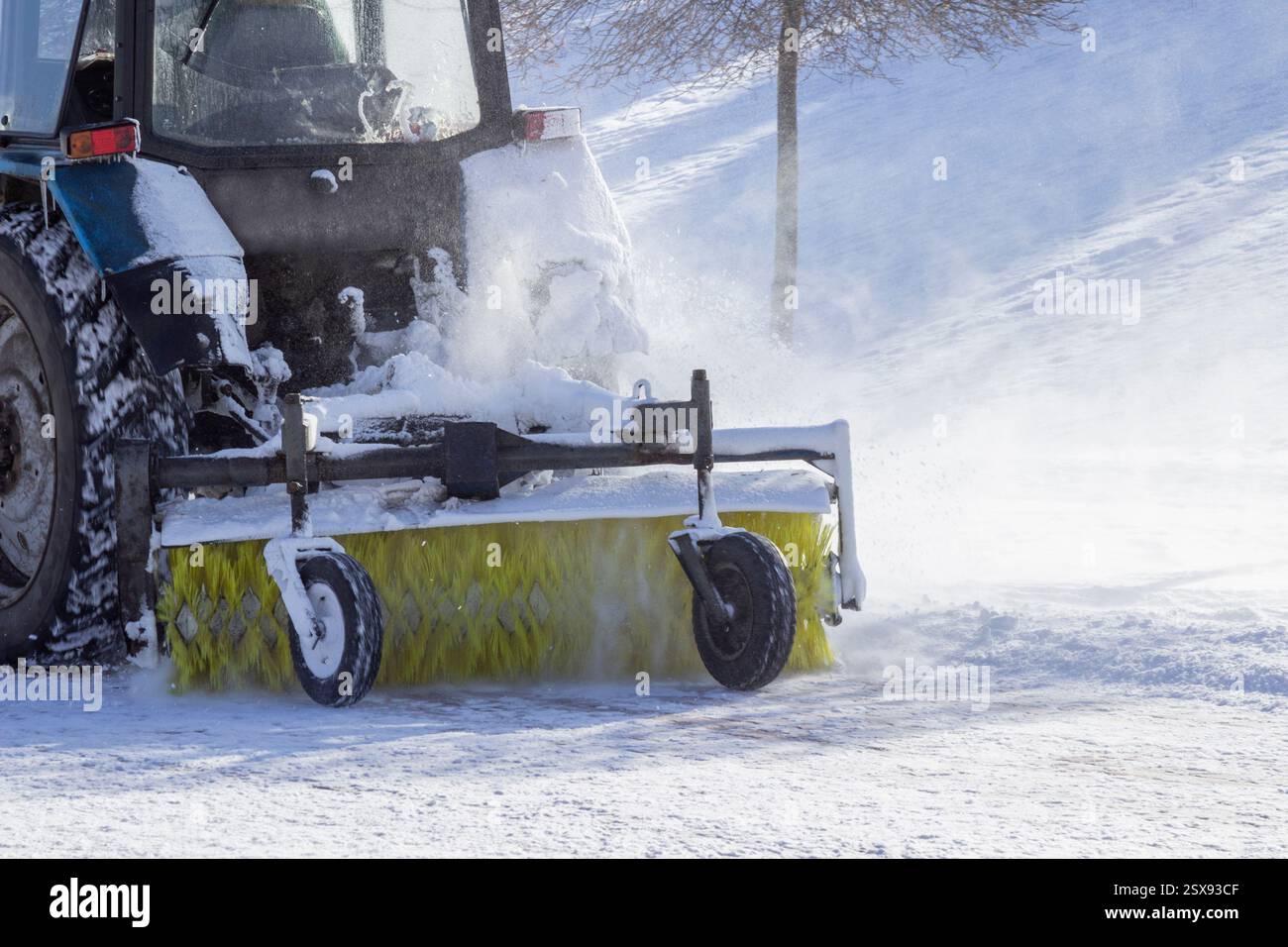Un tracteur sur route enneigée déneigant la neige pendant la chute de neige. Labourage de la route d'hiver. Partie du cadre Banque D'Images