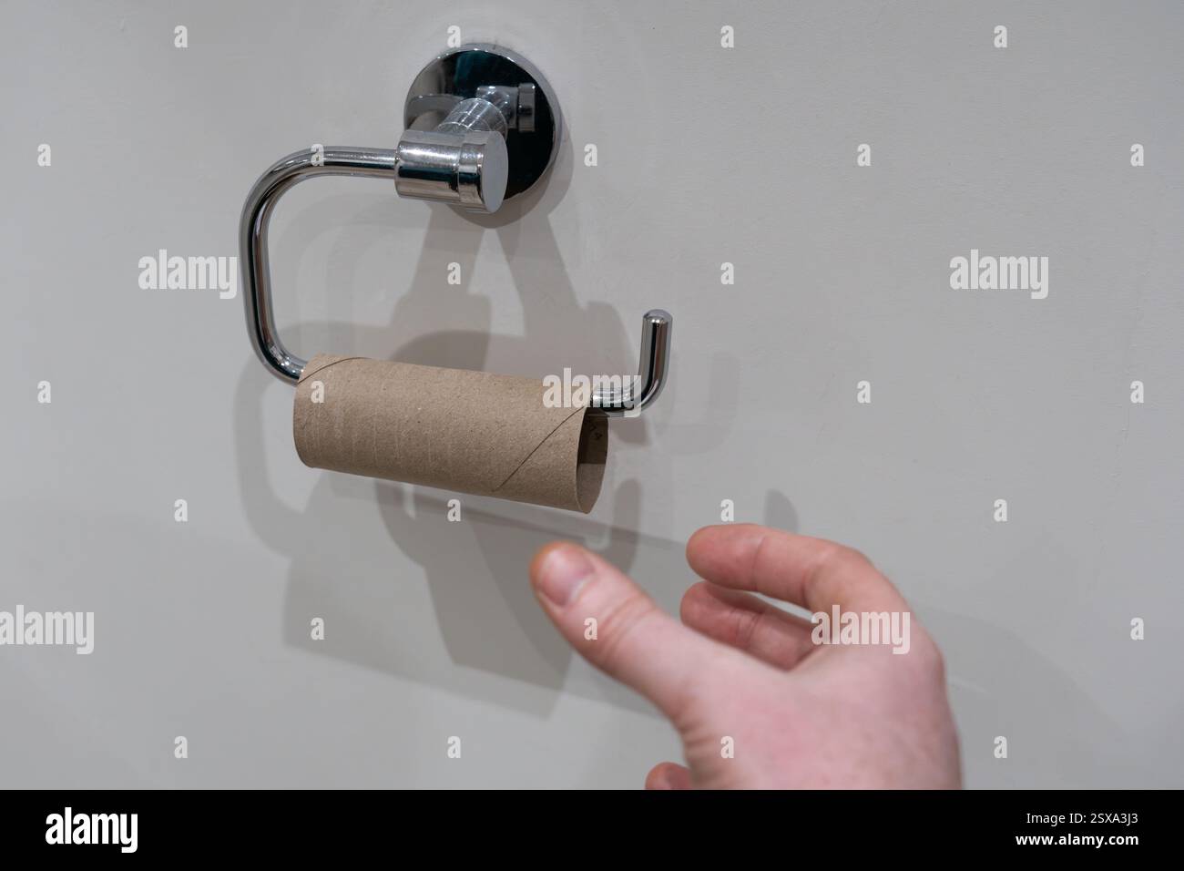 La main d'Aman tend la main pour un rouleau de papier toilette vide, Royaume-Uni. Concept : épuisement, pas de papier toilette, rouleau de loo, rouleau de tourbière, aucun gauche, petit rouleau vide Banque D'Images