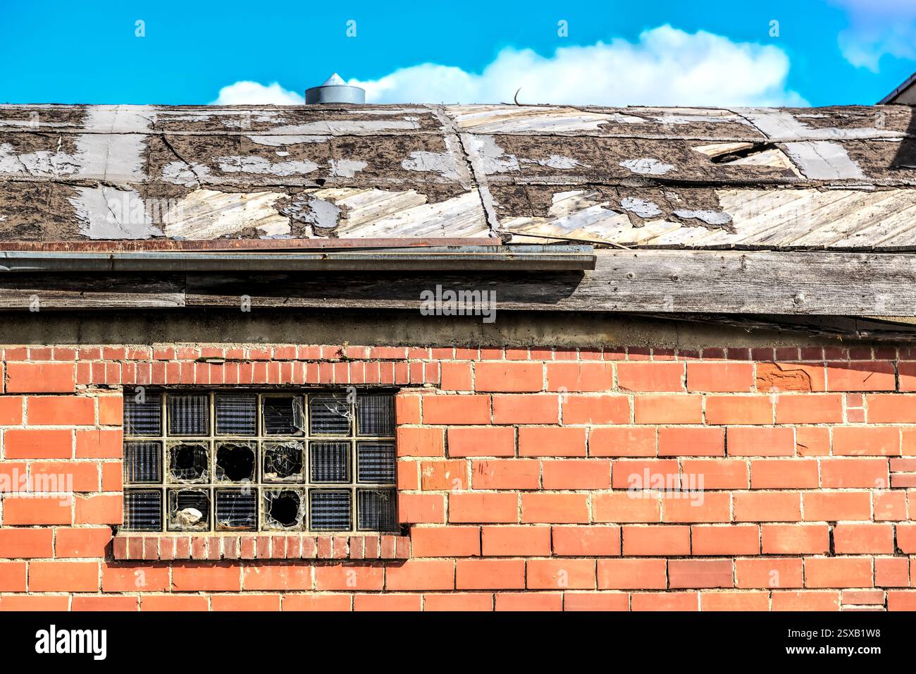 Mur de briques avec une fenêtre et un toit métallique. La fenêtre est cassée et a un trou dedans Banque D'Images